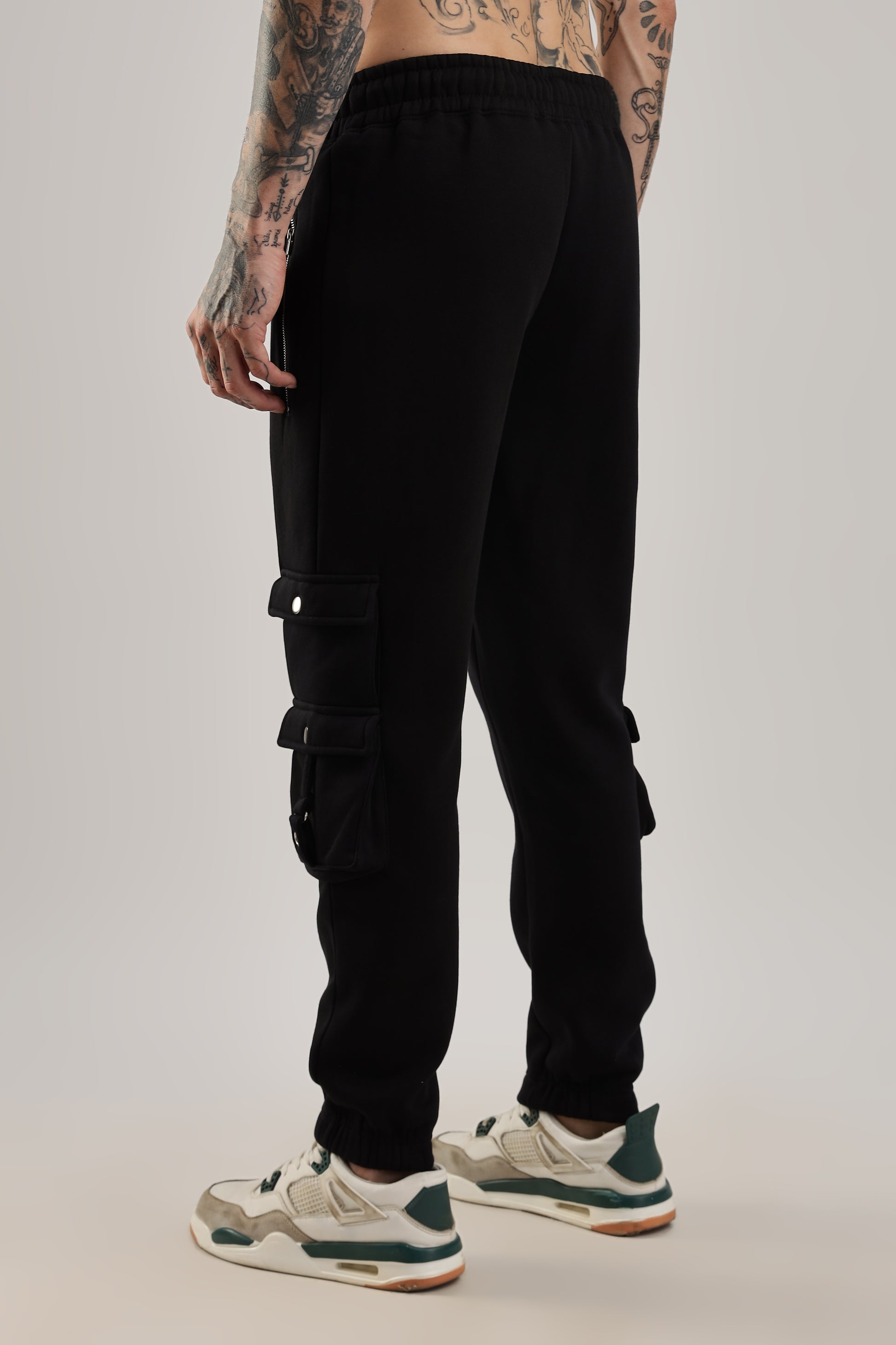 A person standing and facing to the side wearing black ultra joggers with a drawstring waist and tapered leg, along with a pair of sneakers.