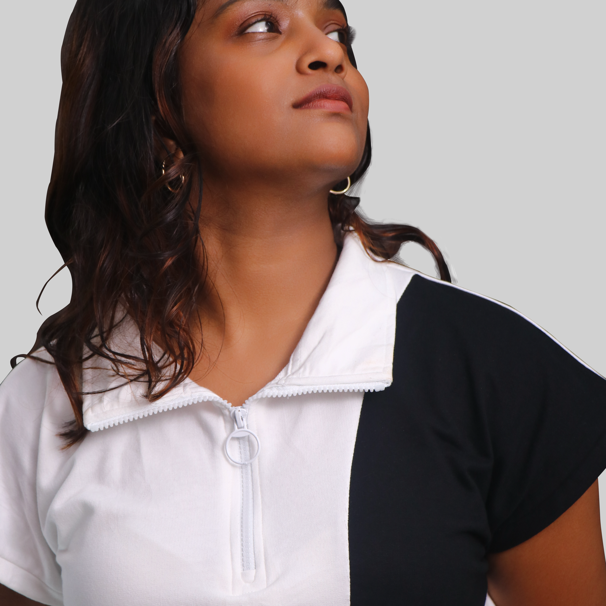 A female model wearing a sleeveless white t-shirt with black panels, featuring a zip top and a crew neck.