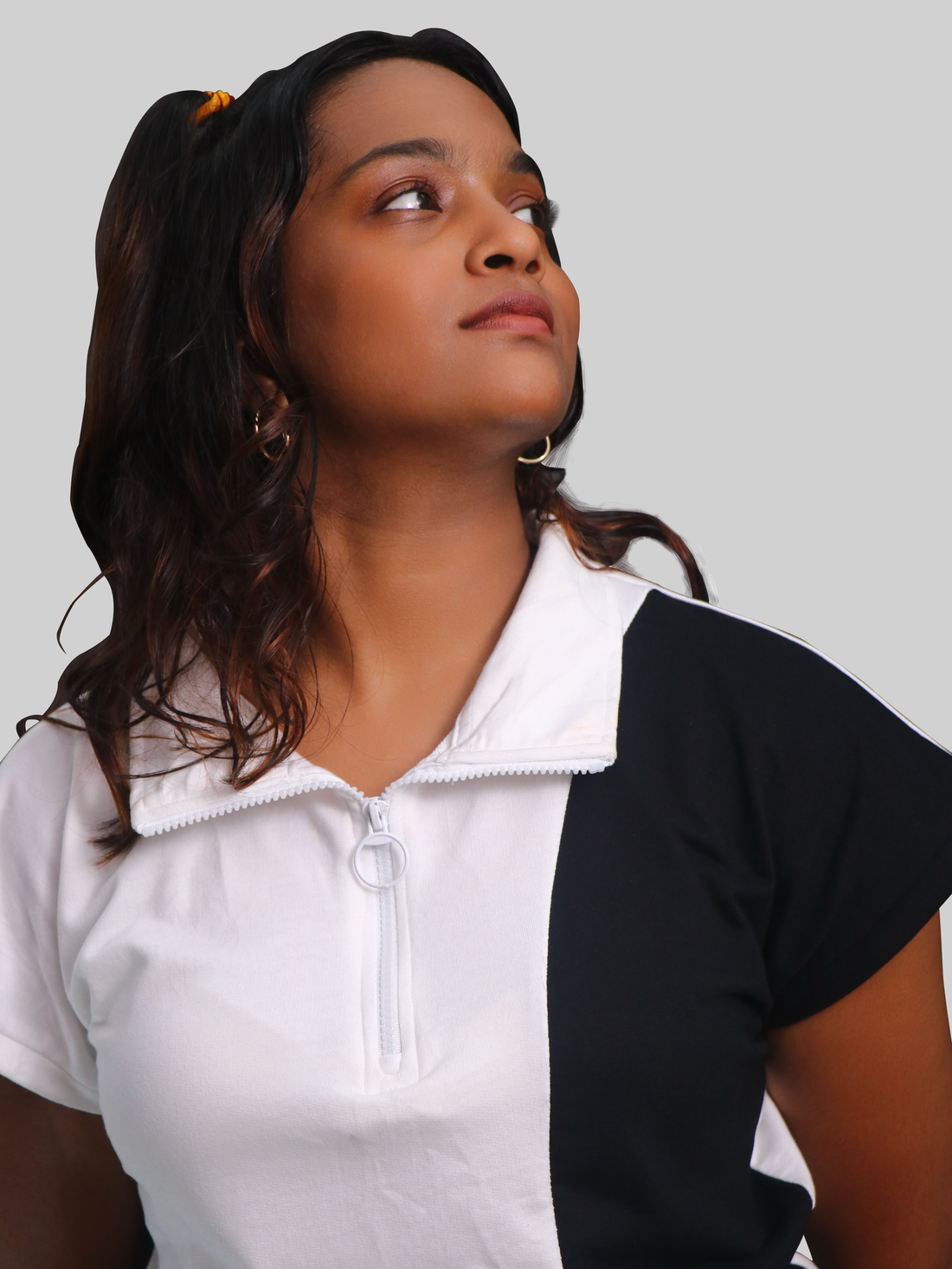 A female model wearing a sleeveless white t-shirt with black panels, featuring a zip top and a crew neck.