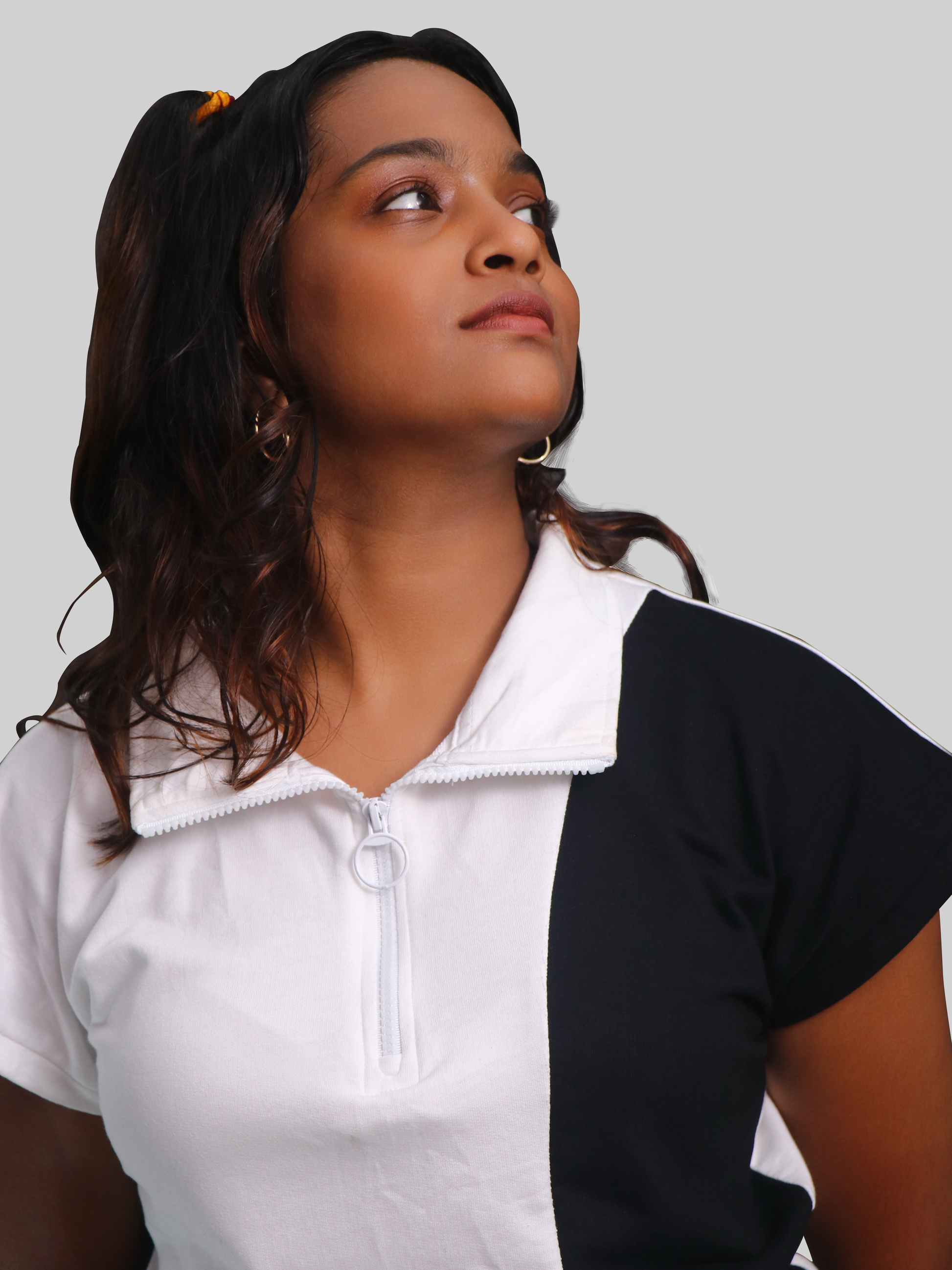A female model wearing a sleeveless white t-shirt with black panels, featuring a zip top and a crew neck.