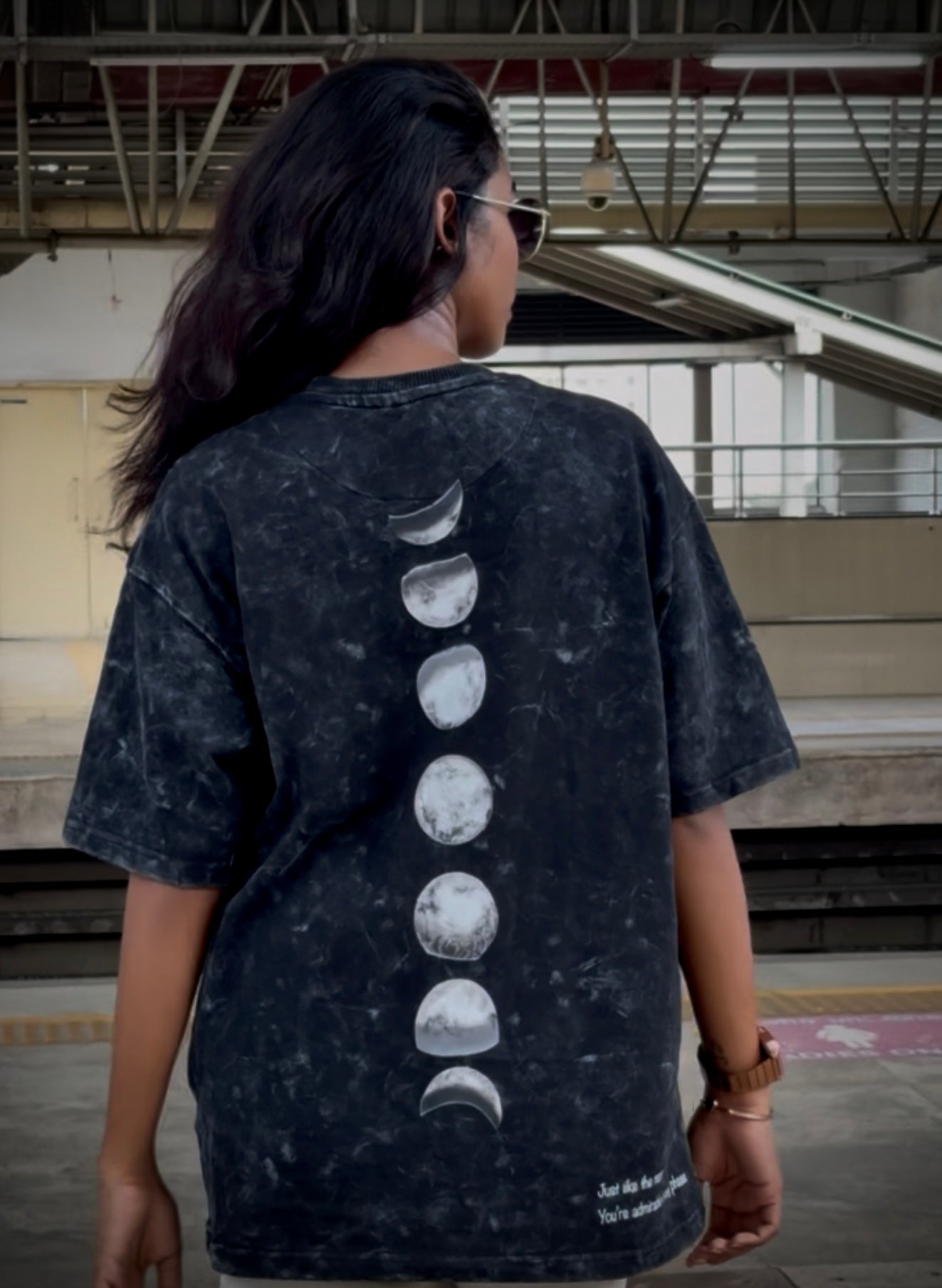Person wearing a black t-shirt with moon phase design in an urban setting