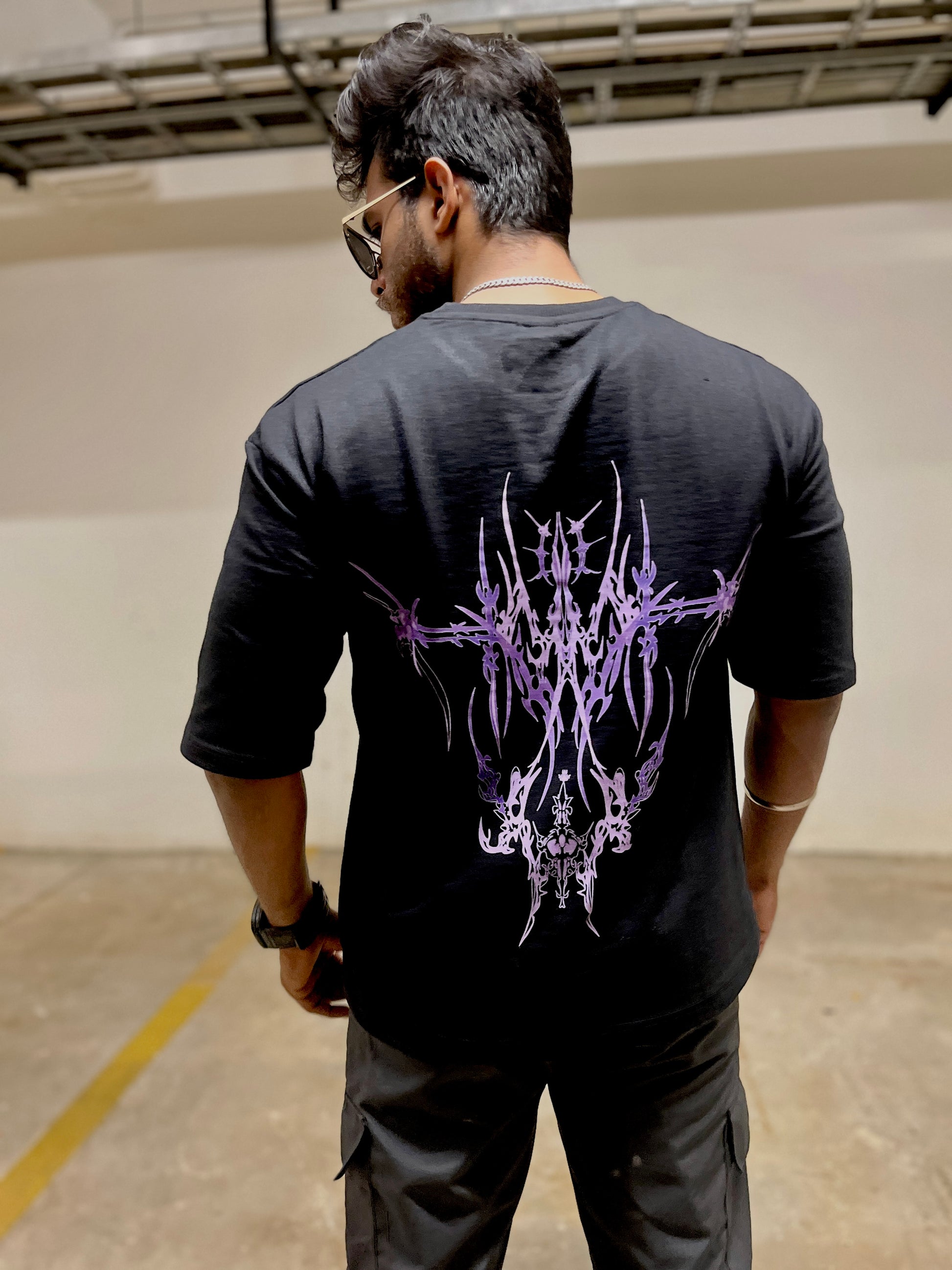 Person wearing a black t-shirt with a purple design on the back in an indoor setting.