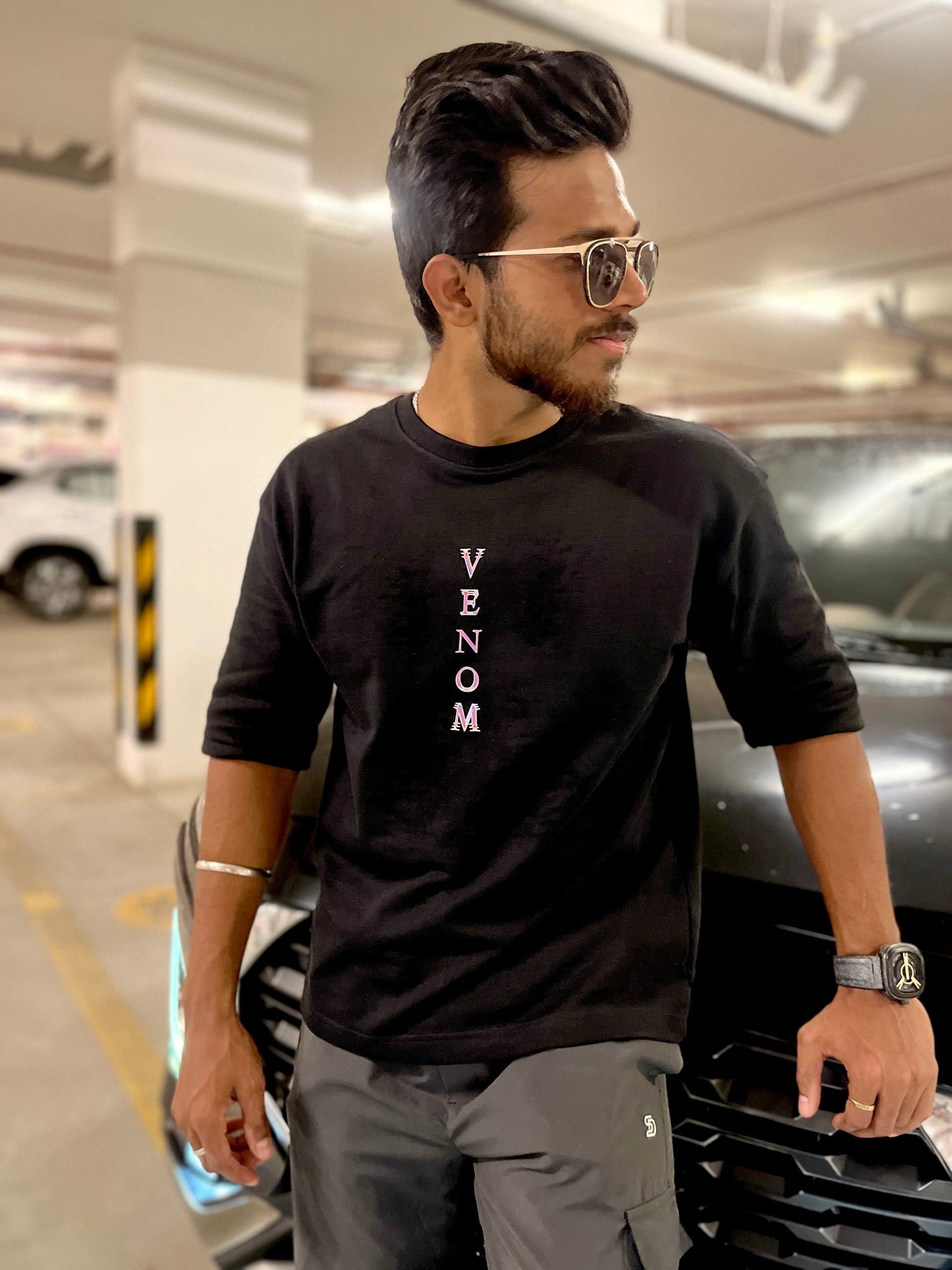 Man wearing a black t-shirt with 'VENOM' text in a parking garage.