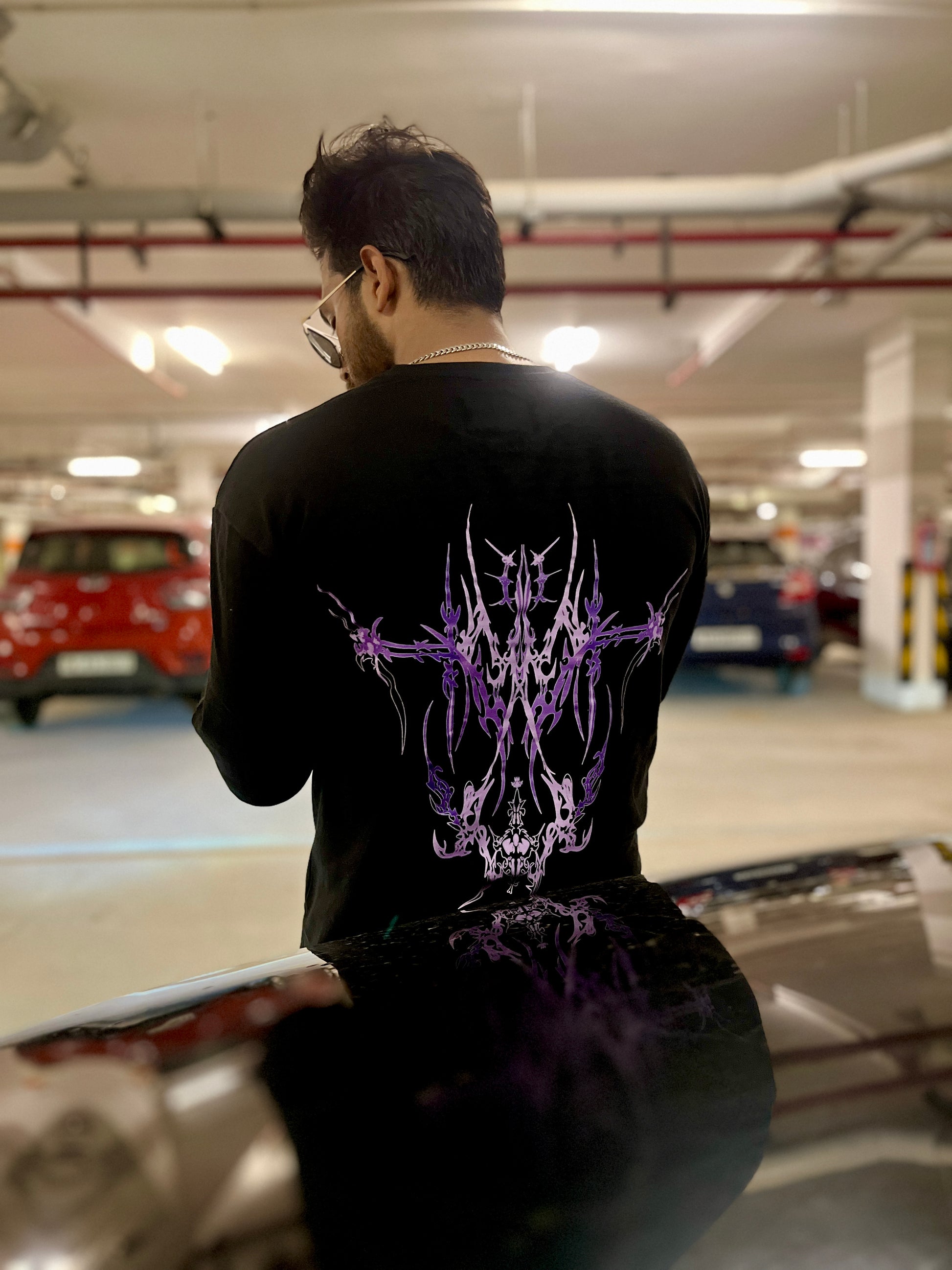 Person wearing a black t-shirt with a purple design in a parking garage