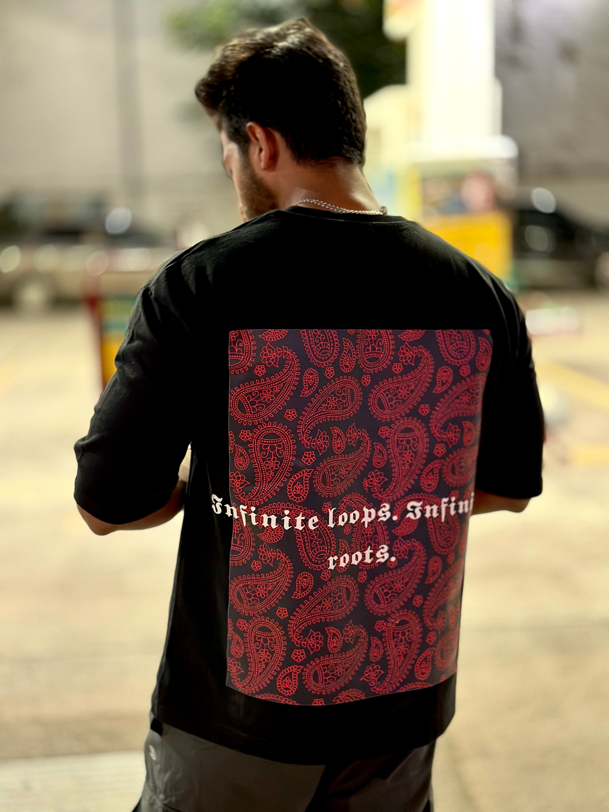 Person wearing a black sweatshirt with red paisley pattern and text on the back, standing outdoors.