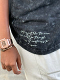 Person wearing a black distressed denim jacket with white text and a rose gold watch.