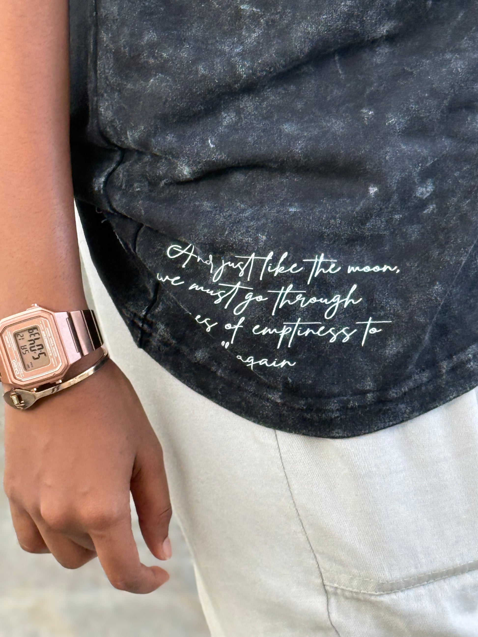Person wearing a black distressed denim jacket with white text and a rose gold watch.