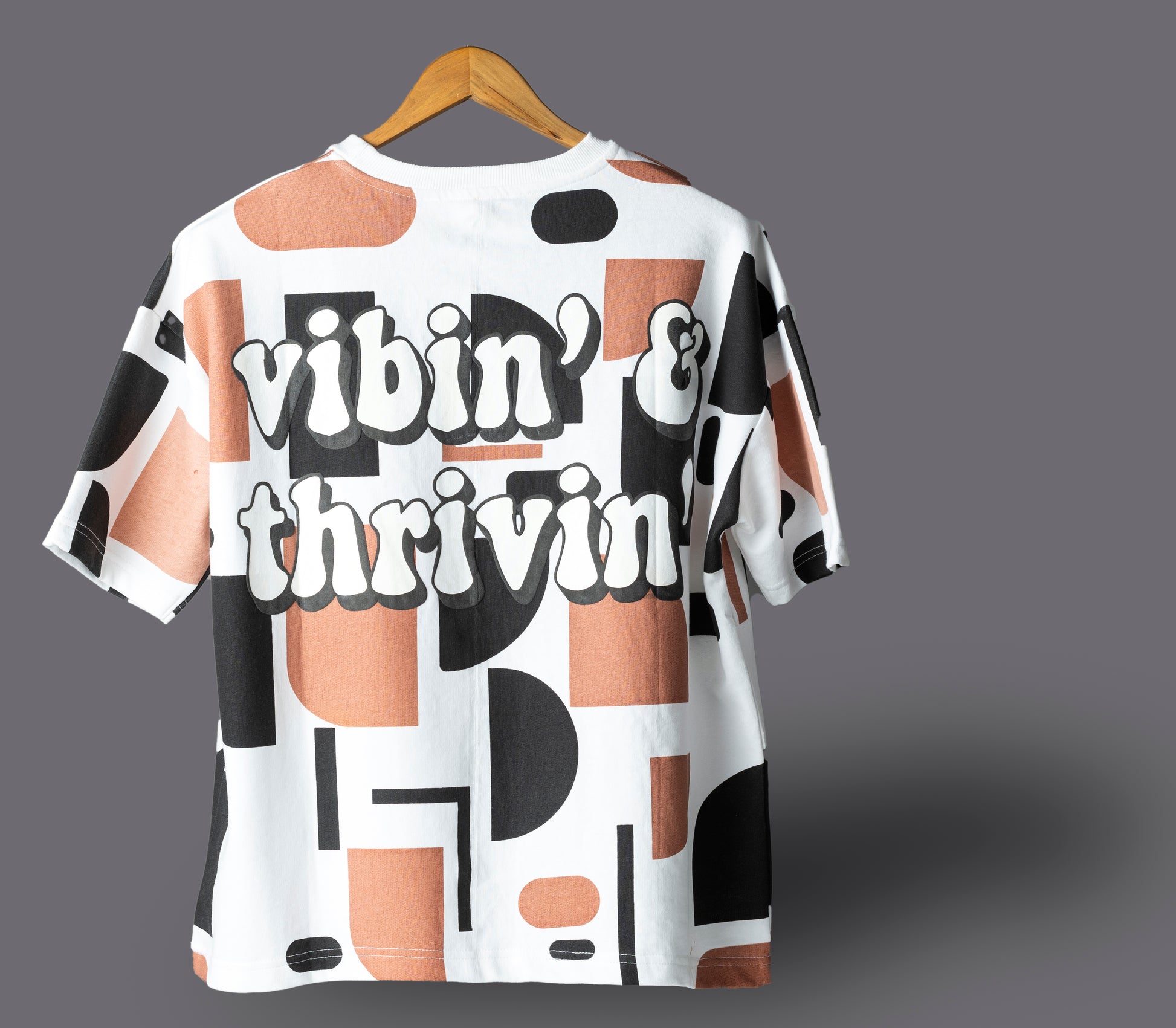 White t-shirt with geometric pattern on a hanger against a gray background