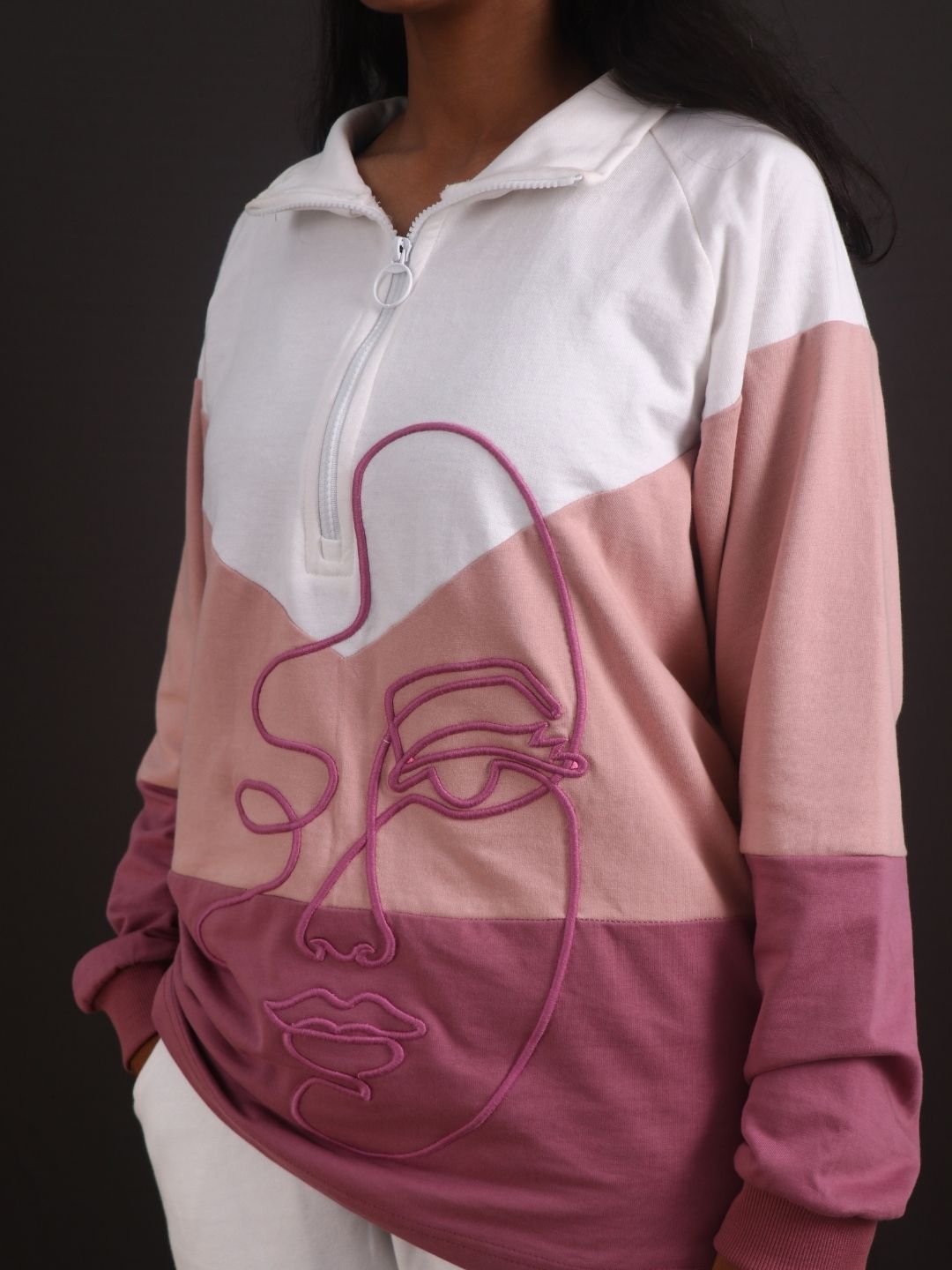 Person wearing a pink and white hoodie with a face design on a dark background