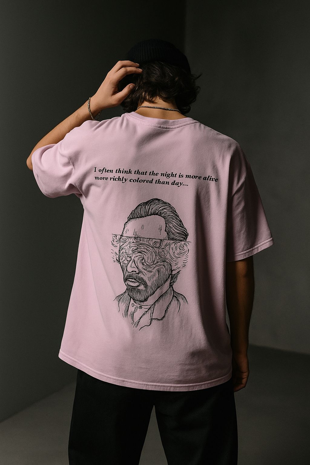 Person wearing a pink t-shirt with a graphic design and text, standing against a dark background.