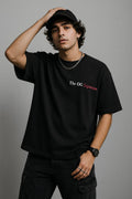 Person wearing a black t-shirt with text, standing against a gray background