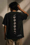 Person wearing a black t-shirt with moon phases design on the back against a plain background