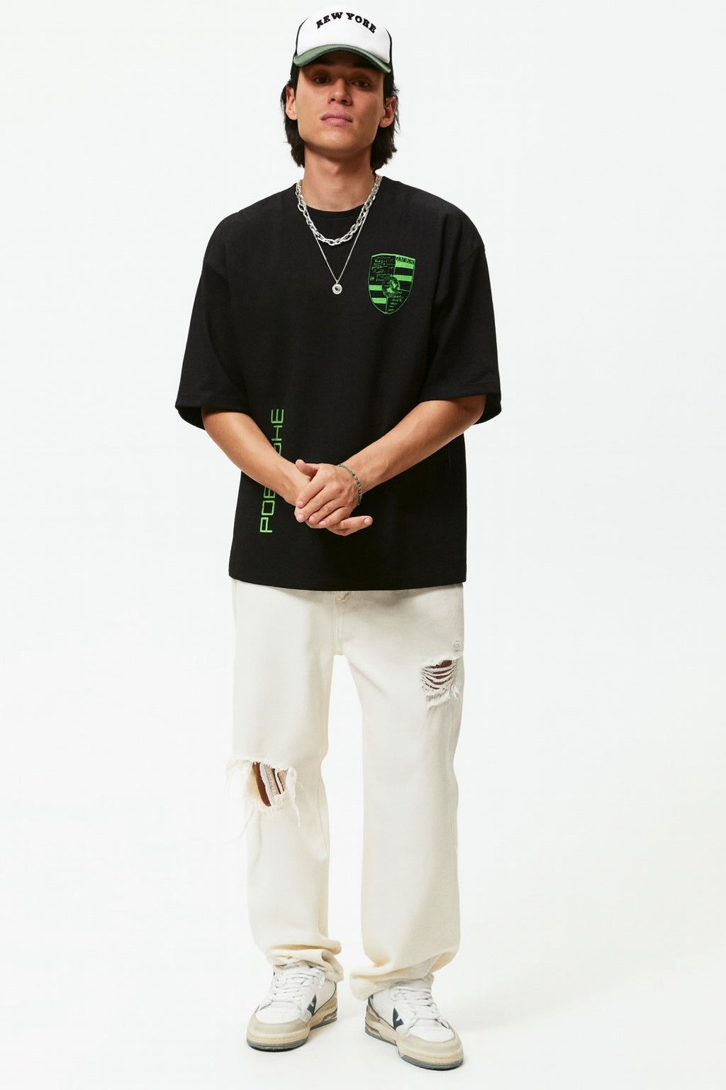 Person wearing a black t-shirt with green logo, white pants, and a white cap on a white background