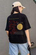 Person wearing a black t-shirt with a graphic design, standing against a plain wall.