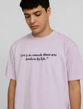 Person wearing a light purple t-shirt with a quote on a plain background